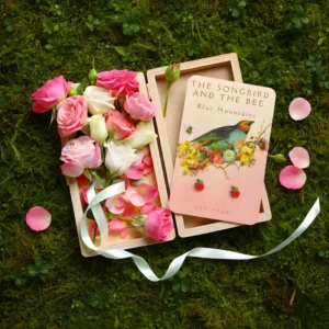 apple gold earrings on a card on a box filled with roses on placed on top of mossy ground