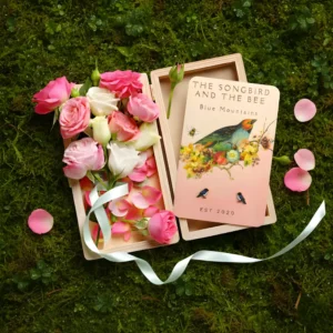 black bird earrings on a card on a box filled with roses on placed on top of mossy ground