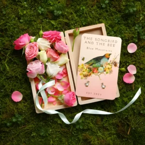 goose gold earrings on a card on a box filled with roses on placed on top of mossy ground
