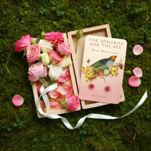 peony gold earrings on a card on a box filled with roses on placed on top of mossy ground